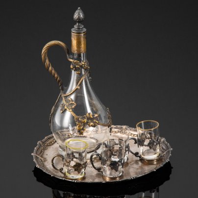 Набор для крепких напитков, состоящий из подноса, графина и четырех стопок на подставках, с растительным декором и дарственной надписью "Въ память отъ любящихъ дѣтей XXV" и "1883.20.10/1908", стекло, металл, серебрение, Plewkiewicz & Co. (Фабрика Романа Плевкевича), Царство Польское, 1908 г.