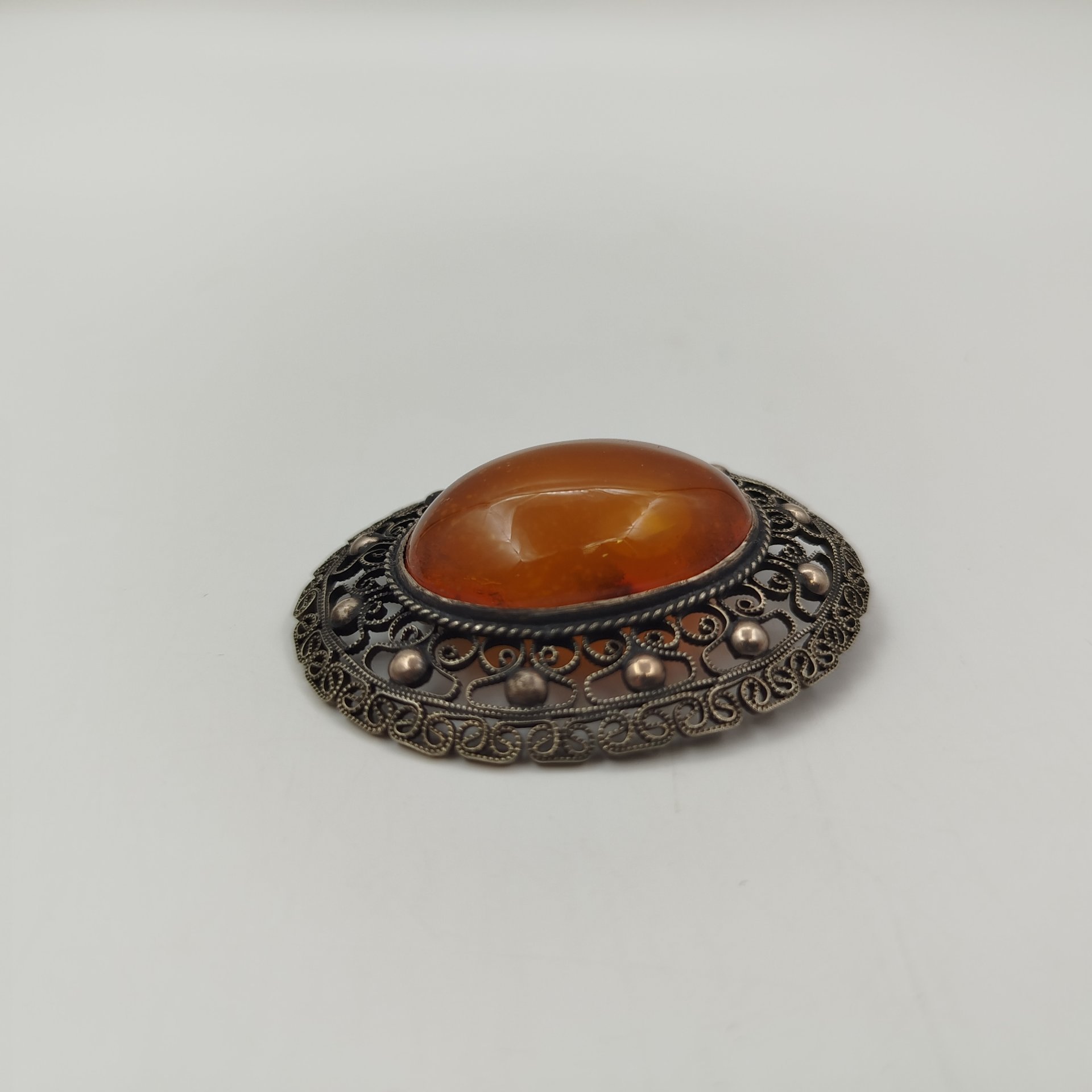 Брошь овальной формы, с янтарной вставкой в центре и ажурным декором