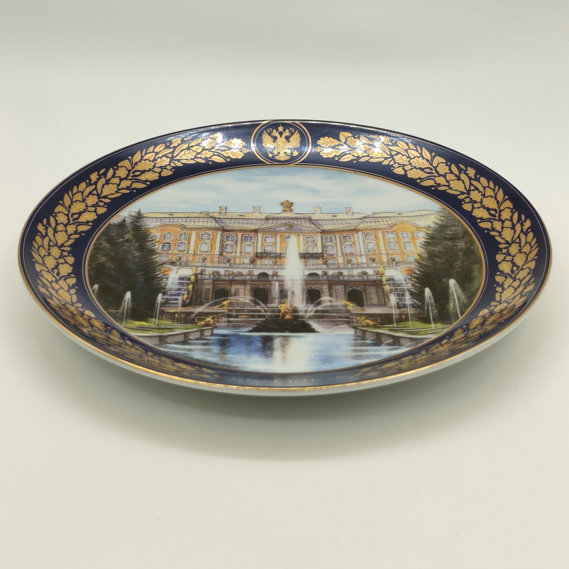 Тарелка настенная "Большой каскад и Большой дворец. Петергоф" из коллекционной серии "Лучшие виды Петергофа", АКМ Сувениры, фарфор, крытье кобальтом, деколь, золочение, Российская Федерация, 2000-2020 гг.