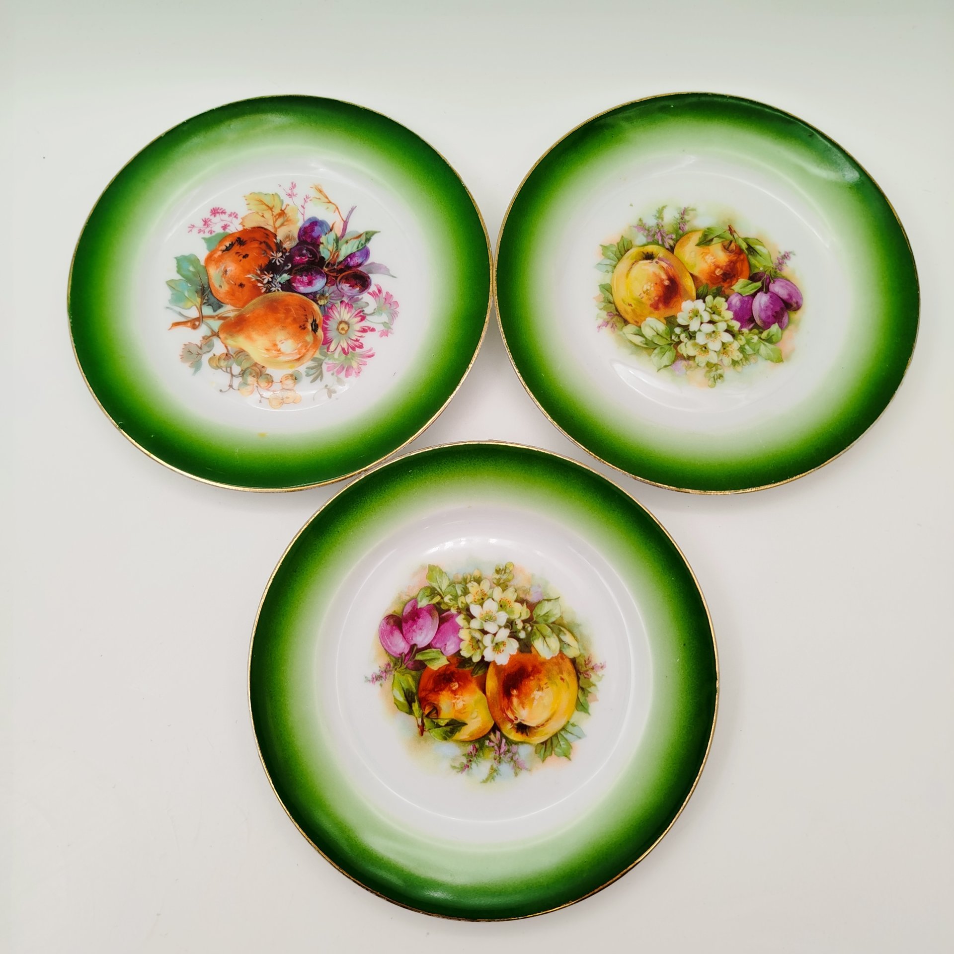 Набор из трех десертных тарелочек с зеленым бортом и изображением фруктов и цветов, фарфор, аэрография, деколь, подрисовка, золочение, Товарищество М.С. Кузнецова, Российская империя, 1880-1917 гг.
