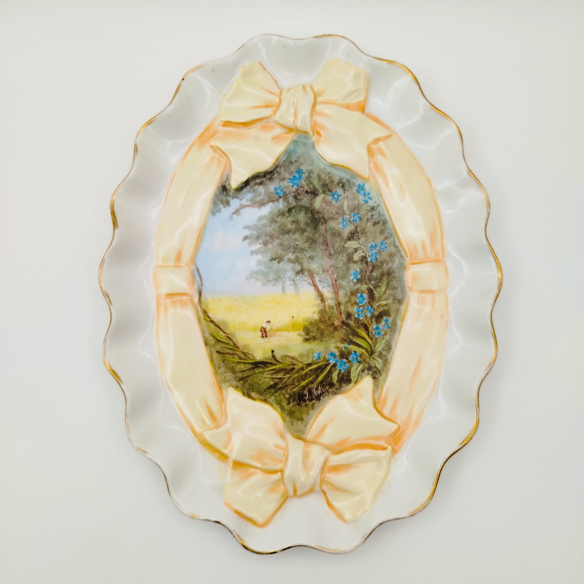 Тарелка (поднос) овальной формы, с фестончатым бортом и сценой сбора урожая в резерве в виде банта, с подписью автора росписи, фарфор, роспись, золочение, Западная Европа, 1890-1930 гг.